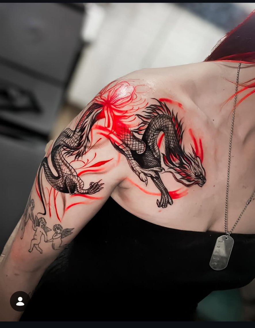 Tatuagem de dragão em preto e cinza com traços vermelhos no ombro